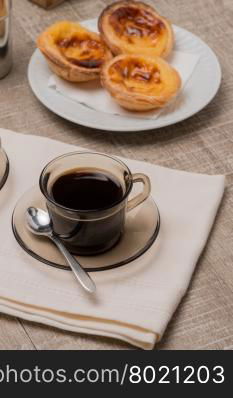 Pasteis de Nata or Portuguese Custard Tarts with black coffee on wooden table.
