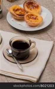 Pasteis de Nata or Portuguese Custard Tarts with black coffee on wooden table.