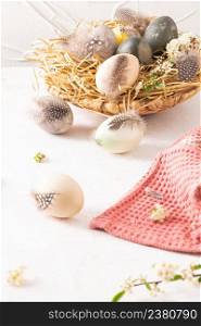 Pastel color Easter eggs feathers and blossom flowers in a nest on a white background. The minimal concept. Card with a copy of the place for the text