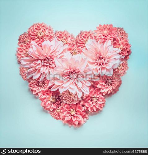 Pastel color heart made of lovely pink flowers on turquoise blue background, top view. Love, wedding or Valentines day concept. Layout for greeting card
