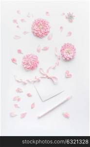 Pastel color mock up with pink flowers and petals, blank paper card with ribbon and point pen on white desktop background, top view. Layout of greeting card for Mothers day, wedding or happy event