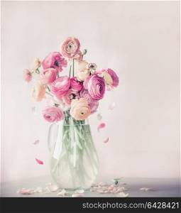 Pastel color ranunculus flowers bouquet with falling petals in glass vase on table, front view