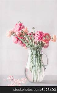 Pastel color ranunculus flowers bunch in glass vase on table, front view