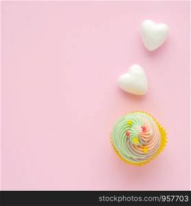 Pastel cupcake and white hearts on pink background with copy space for text, birthday, anniversary greeting card background, flat lay, top view
