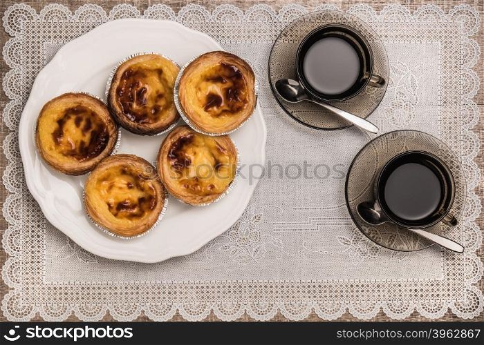 Pastel de nata, typical Portuguese egg tart pastries and black coffee on a set table. Top view with copy space