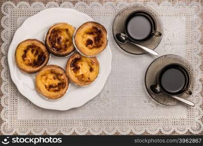 Pastel de nata, typical Portuguese egg tart pastries and black coffee on a set table. Top view with copy space