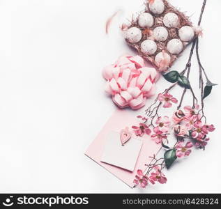 Pastel pink Easter composing with greeting card mock up with blossom decoration, feathers, eggs in carton box on white desk background, top view, flat lay