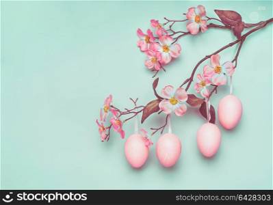 Pastel pink Easter eggs hanging on spring blossom branch at blue turquoise background, copy space for greeting or invitation