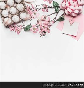 Pastel pink Easter greeting card mock up with blossom decoration, eggs in carton box on white desk background, top view, flat lay, border