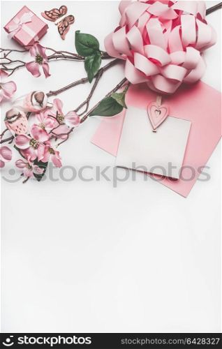 Pastel pink greeting card mock up with blossom decoration, hearts, little gift box and bow on white desk background, top view, flat lay. Wedding invitation, Girls birthday or Mother day concept
