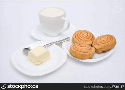 pastry, butter and a cup of milk on three saucers