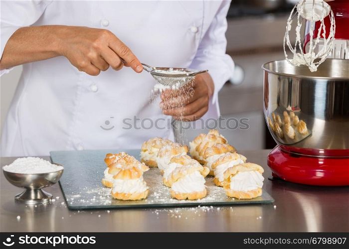 Pastry chef decorating with icing sugar some profiteroles