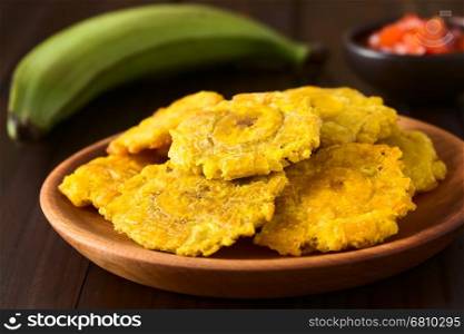 Patacon or toston, fried and flattened pieces of green plantains, a traditional snack or accompaniment in the Caribbean, photographed on dark wood with natural light (Selective Focus, Focus on the front of the top patacon)