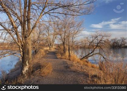 pathway on a narrow dike between lakes, late fall or winter scenery with ice cover, Riverbend Ponds Nature Area, Fort Collins, Colorado
