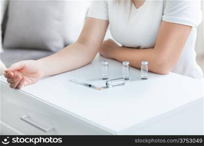 Patient holding hand on table with syringe and drug bottles
