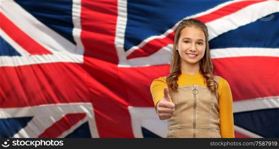 patriotism, gesture and people concept - smiling young teenage girl showing thumbs up over british flag background. teenage girl showing thumbs up over british flag
