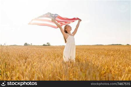 patriotism, independence day and country concept - happy smiling young girl holding national american flag waving over cereal field. girl with american flag waving over cereal field