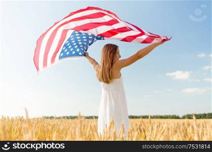 patriotism, independence day and country concept - happy smiling young girl holding national american flag waving over cereal field. girl with american flag waving over cereal field