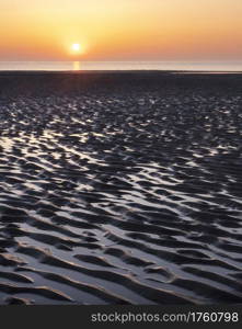 pattern in sand and colorful reflection of setting sun in water during sunset on beach