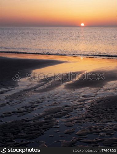 pattern in sand and colorful reflection of setting sun in water during sunset on beach