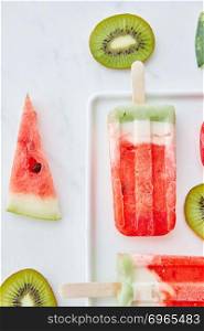 Pattern of fresh pieces of fruit kiwi, watermelon and ice cream lolly in a plate on a gray marble background with space for text. Summer dessert. Flat lay. Appetizing composition of ice lolly on a stick and juicy pieces of watermelon and kiwi on a gray marble background with copy space. Flat lay