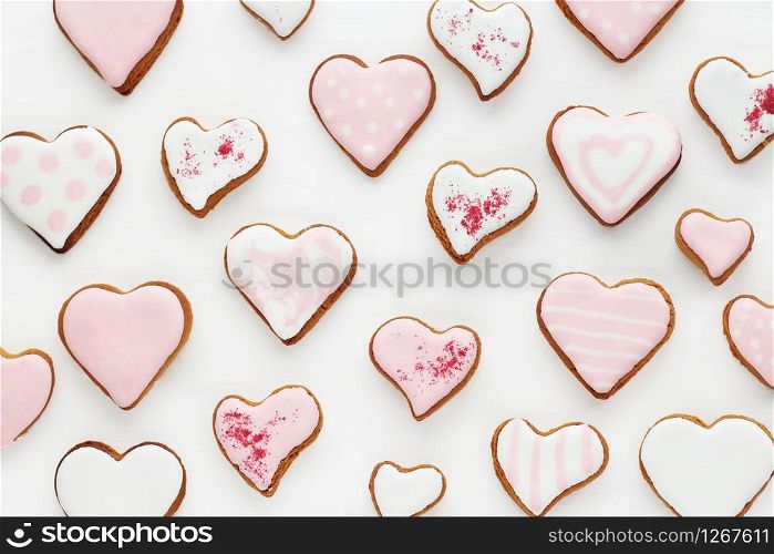 pattern of gingerbread cookies in the shape of a heart decorated with white and pink glaze on a white wooden background.