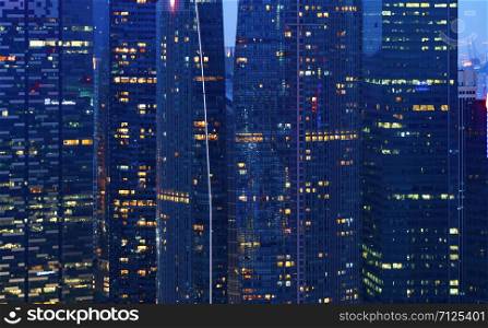 Pattern of office buildings windows illuminated at night. Lighting with Glass architecture facade design with reflection in urban city, Downtown Singapore City in financial district.