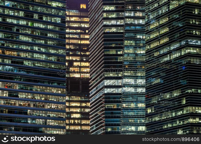 Pattern of office buildings windows illuminated at night. Lighting with Glass architecture facade design with reflection in urban city, Downtown Singapore City in financial district.