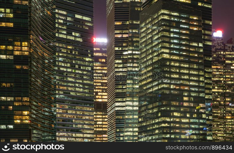 Pattern of office buildings windows illuminated at night. Lighting with Glass architecture facade design with reflection in urban city, Downtown Singapore City in financial district.