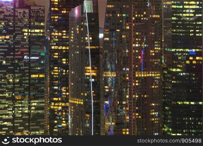 Pattern of office buildings windows illuminated at night. Lighting with Glass architecture facade design with reflection in urban city, Downtown Singapore City in financial district.