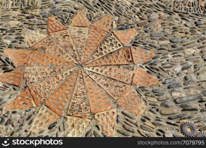 Patterned floor with sea pebbles red bricks and metal gears in the park Montjuic, Barcelona, Catalonia, Spain