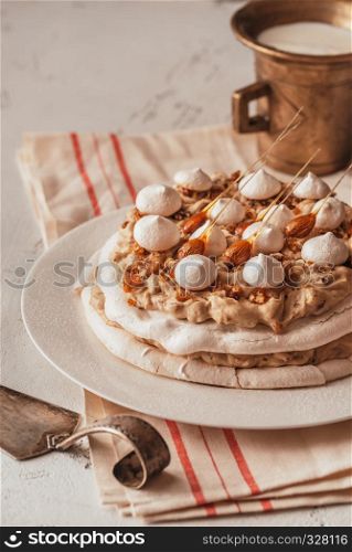 Pavlova cake with caramel and almonds on the wooden background