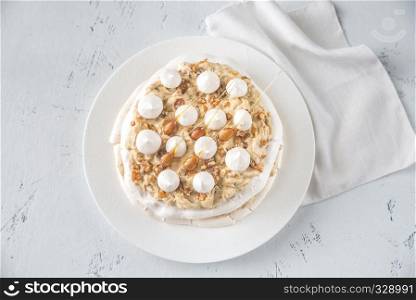 Pavlova cake with caramel and almonds on the wooden background