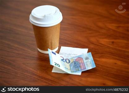 payment and consumerism concept - coffee drink in paper cup, bill and money on table