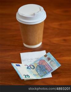 payment and consumerism concept - coffee drink in paper cup, bill and money on table