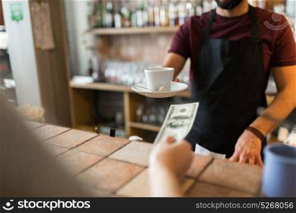 payment, people and service concept - man or bartender with cup serving customer paying money at coffee shop. man or bartender serving customer at coffee shop