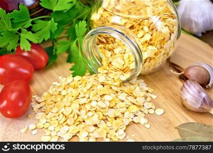Pea flakes in a glass jar, parsley, garlic, tomatoes, a clay pot on a wooden boards background