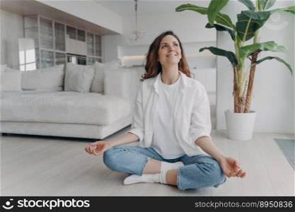 Peace of mind and mental health concept. Young european woman is practicing yoga on floor and smiling. Meditation, consciousness and relaxation at home. Posture exercise, lotus asana.. Peace of mind and mental health concept. Young european woman practicing yoga on floor and smiling.