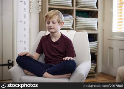 Peaceful Boy Meditating Sitting In Chair In Bedroom At Home