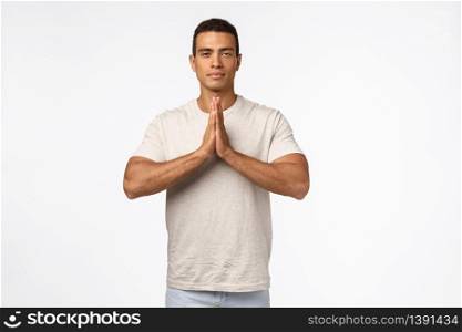 Peaceful good-looking strong, athletic young man in casual t-shirt, press hands together over chest in namaste, nirvana pose, look patient and calm, release stress in meditation, practice yoga.. Peaceful good-looking strong, athletic young man in casual t-shirt, press hands together over chest in namaste, nirvana pose, look patient and calm, release stress in meditation, practice yoga