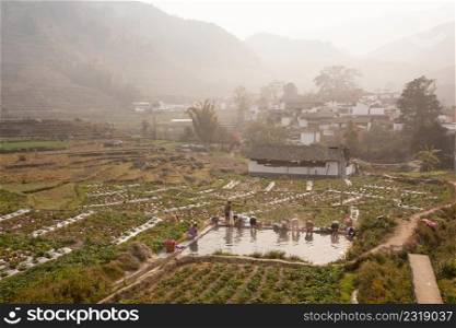 Peaceful village. Scenic ancient village landscape, a group of chinese woman washing at the old pool in potato?s field in the mist. Mountains in the mist backgrounds. Yunnan, rural of South China. Soft morning light.