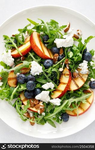 Peach, blueberry and arugula fresh fruit salad with cheese and almond nuts, top view