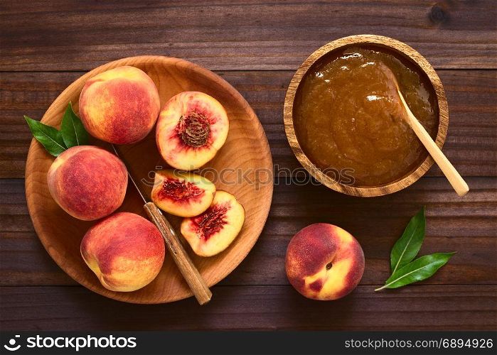 Peach jam or jelly in wooden bowl with fresh ripe peach fruits on wooden plate on the side, photographed overhead on dark wood with natural light. Peach Jam or Jelly