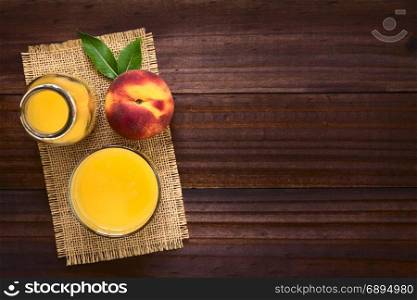Peach juice or nectar in glass and in bottle with fresh ripe peach fruit on the side, photographed overhead on dark wood with natural light (Selective Focus, Focus on the top of the juice and the top of the whole fruit). Peach Juice or Nectar