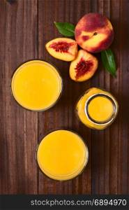 Peach juice or nectar in glasses and in bottle with fresh ripe peach fruits on the side, photographed overhead on dark wood with natural light (Selective Focus, Focus on the top of the juices and the top of the whole fruit). Peach Juice or Nectar