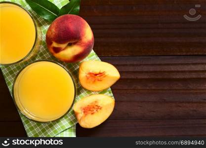 Peach juice or nectar in glasses with fresh ripe peach fruit on the side, photographed overhead on dark wood with natural light (Selective Focus, Focus on the top of the juices and the top of the whole fruit). Peach Juice or Nectar