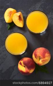 Peach juice or nectar in glasses with fresh ripe peach fruits on the side, photographed overhead on slate with natural light (Selective Focus, Focus on the top of the juice and the top of the whole fruits). Peach Juice or Nectar