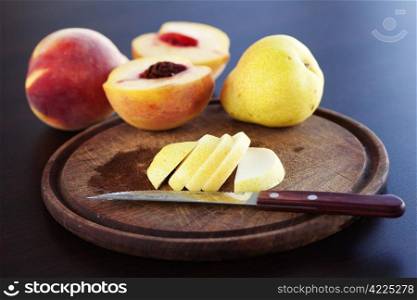 peach, pear and a knife on a cutting board