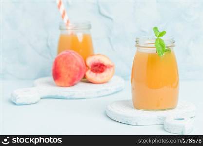 Peach smoothie in glass jars with fresh ripe fruits and green mint leaves on blue pastel background - raw sweet dessert or breakfast drink for healthy organic eating concept.. Peach smoothie in glass jars with fresh ripe fruits and green mint leaves on blue pastel background.