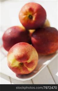 Peaches over white plate, over white wooden table, vertical image
